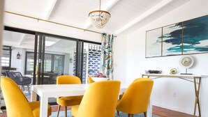 A dining area with a white table and yellow chairs, a chandelier, and a large abstract painting on the wall. - St. Croix - Villa Views at Hermon Hill! (St Croix)