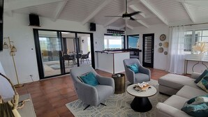 A spacious living room with a sofa, armchairs, and a coffee table. There is a sliding glass door leading to a balcony. - St. Croix - Villa Views at Hermon Hill! (St Croix)