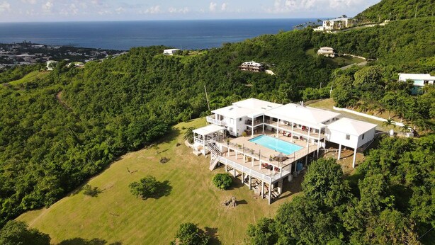 A large, modern house with a swimming pool, surrounded by lush greenery and overlooking a coastal area. - St. Croix - Villa Views at Hermon Hill! (St Croix)