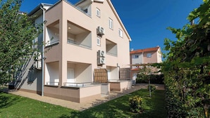 Un immeuble résidentiel de deux étages, doté d’un toit plat, de balcons et d’un petit jardin.