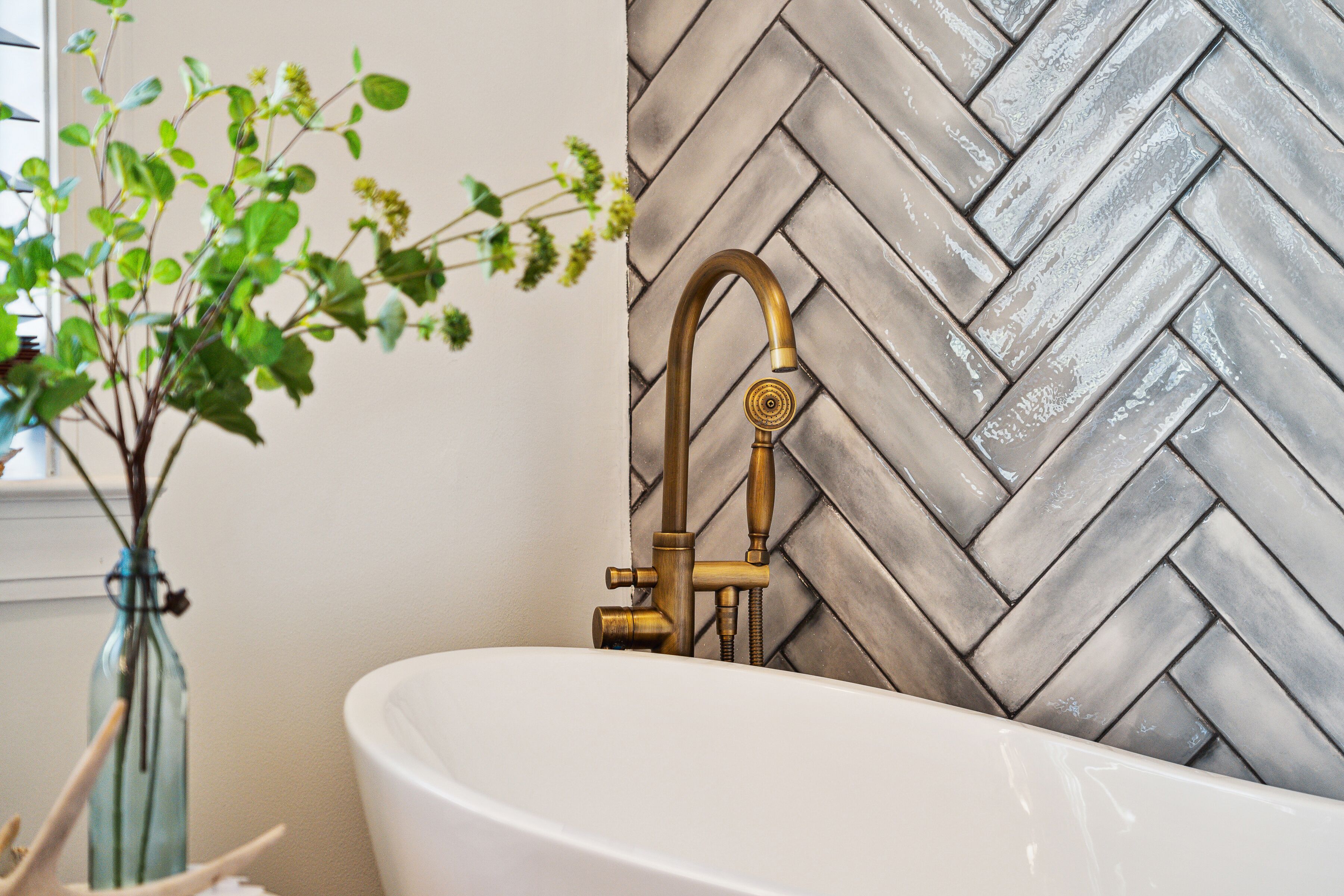 Un bagno con una vasca da bagno bianca, un rubinetto in ottone e un rivestimento murale a motivi a spina di pesce.