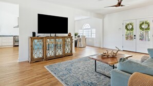A spacious living room with a large flat-screen TV, wooden cabinets, a blue patterned rug, and a grey sofa. - NEW Waterfront, private dock, fully updated Johns Island home (Johns Island)