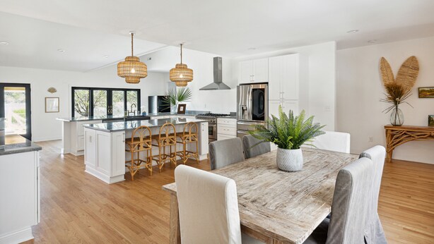A spacious kitchen with white cabinetry, a central island, and a dining area with a wooden table and chairs. - NEW Waterfront, private dock, fully updated Johns Island home (Johns Island)