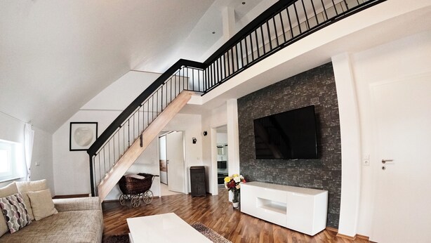 A modern living room with a staircase, a flat-screen TV, and a white entertainment unit.