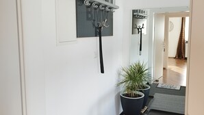 A hallway with a coat rack, a potted plant, and a mat leading to a door.
