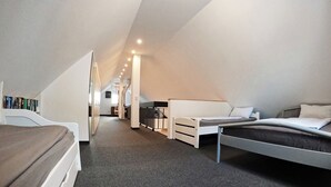 A modern, well-lit attic bedroom with a sloped ceiling, two beds, a small desk, and a bookshelf.