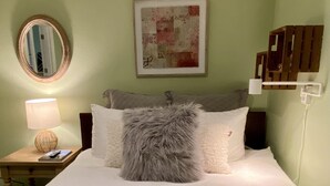 Ein ordentlich bezogenes Bett mit Kissen, einer Nachttischlampe und einem Holfnachtkästchen.