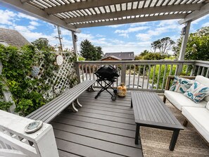 En overdækket terrasse med grill, siddepladser og et hvidt hegn med slyngplanter.