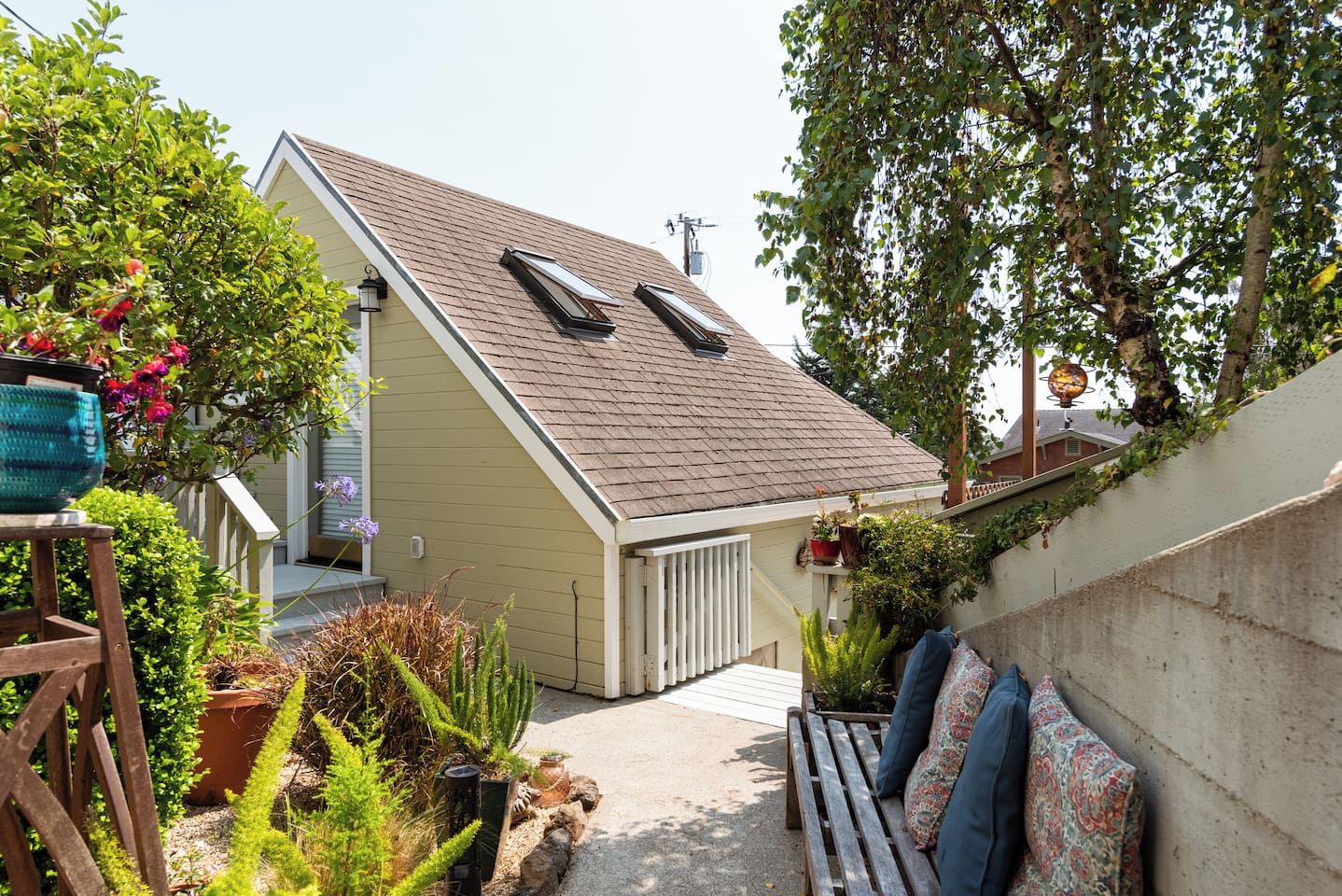 A residential property with a sloped roof, a covered porch, and a small garden area with various plants and a bench.