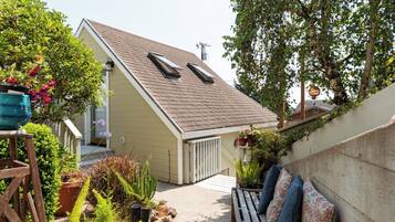 A residential property with a sloped roof, a covered porch, and a small garden area with various plants and a bench.