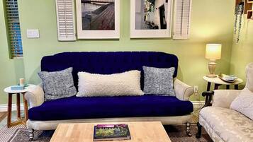 Una sala de estar con un sofá azul, una mesa de centro de madera y dos cuadros en la pared.