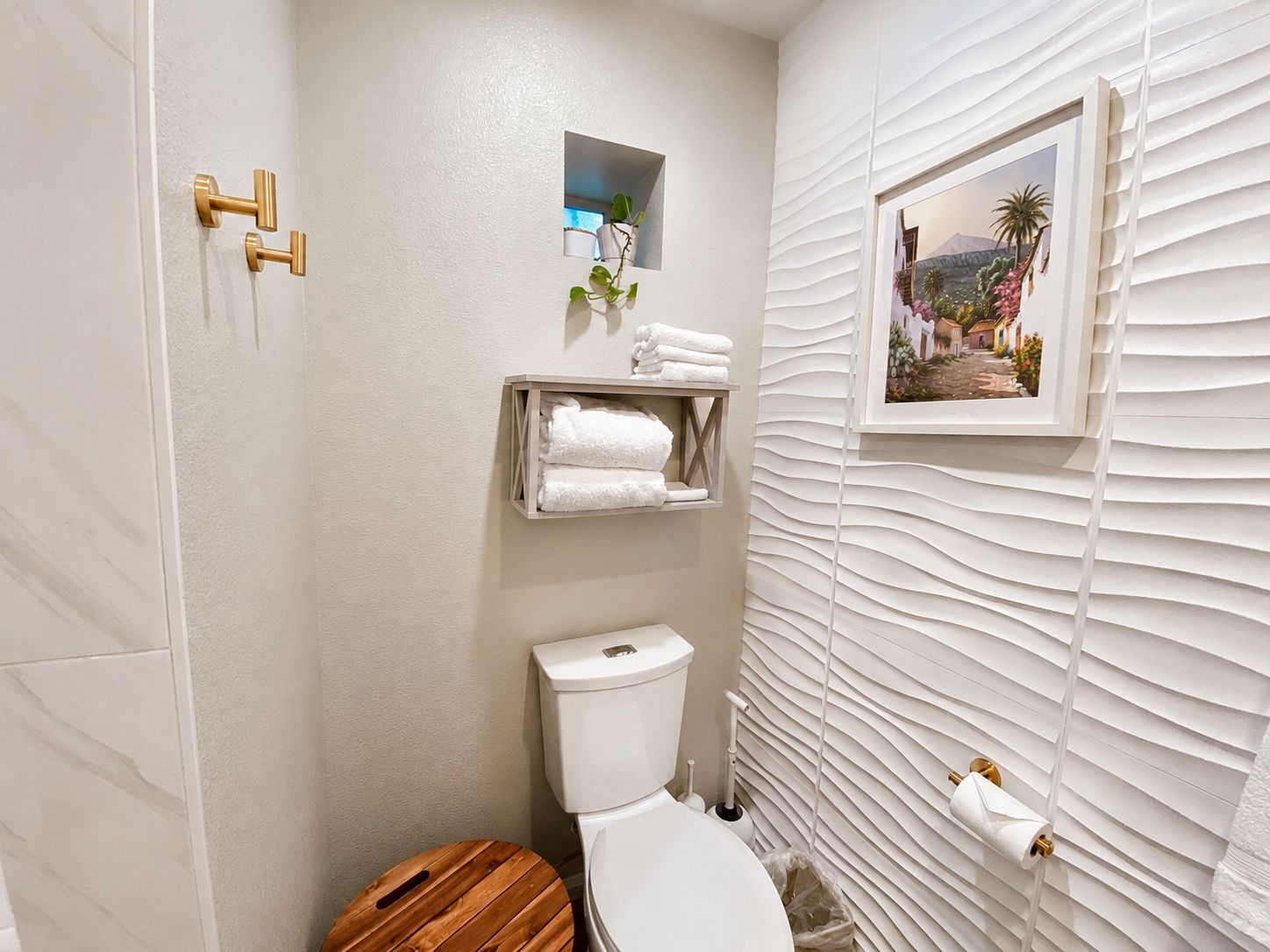 Un baño con inodoro blanco, tocador de madera, perchero y un cuadro en la pared.