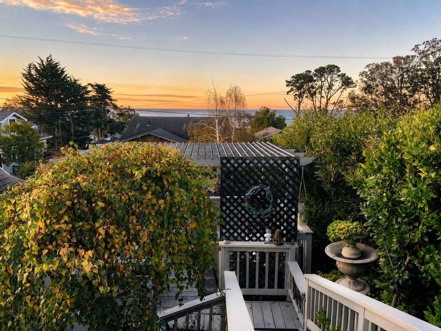 A residential deck with a view of houses and trees, a lattice fence, and a bird bath.
