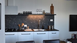 Une cuisine moderne avec un plan de travail noir, des armoires blanches et un luminaire suspendu.
