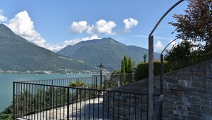 Un balcon doté d’un mur en pierre et d’une rambarde en métal, offrant une vue sur un lac et des montagnes.