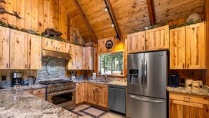 Cocina de cabaña de madera con encimeras de granito, electrodomésticos de acero inoxidable y un ventanal con vistas a un bosque.