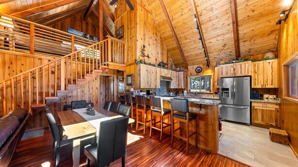 Interior de una cabaña de madera con comedor, cocina y escalera.