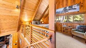 Interior acogedor de una cabaña con habitación en altillo, escalera de madera, sofá y un ventanal con vista a los árboles.