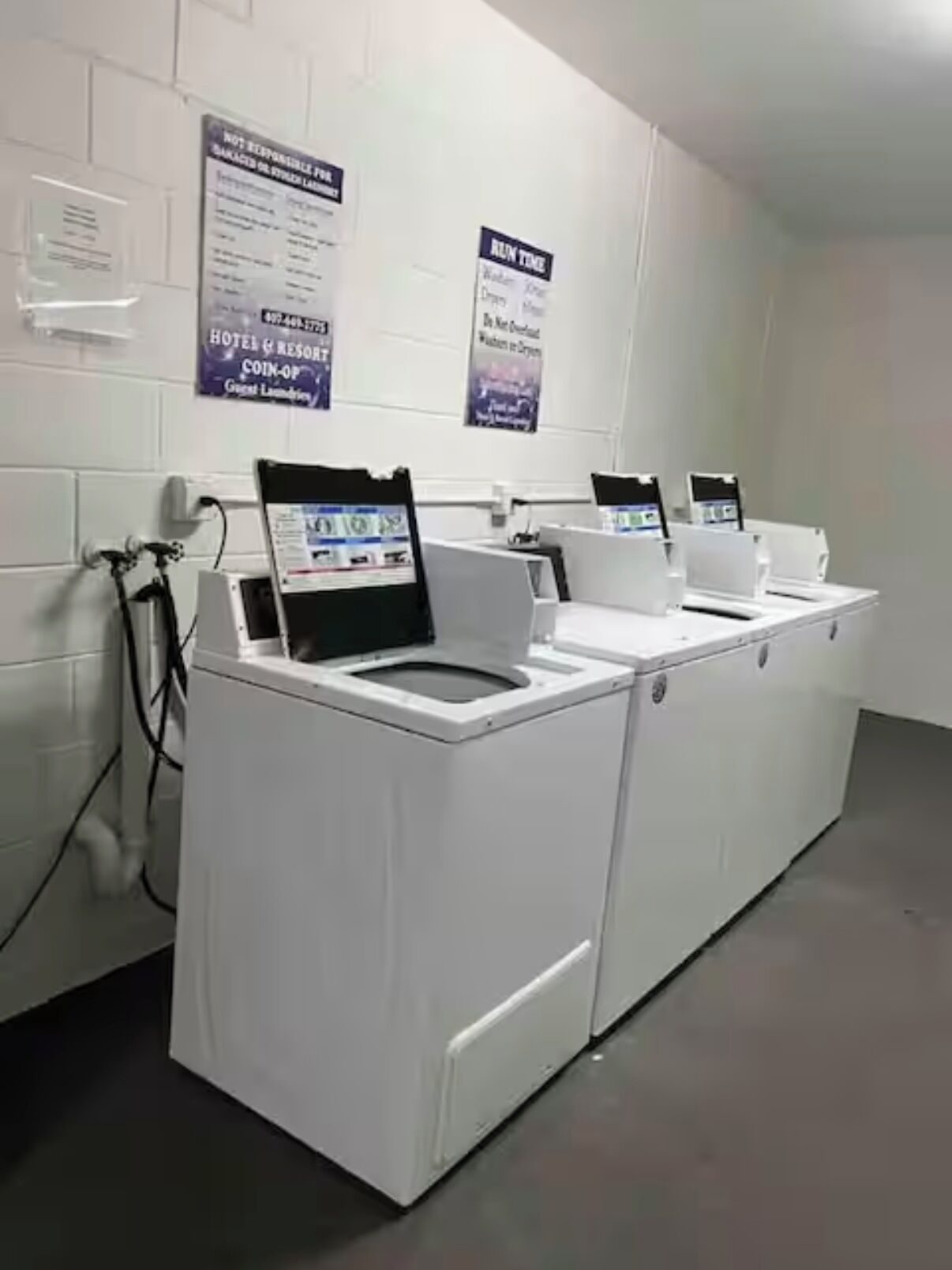 Een hotelwasserij met meerdere wasmachines en drogers, een waterfontein en informatieposters aan de muur.