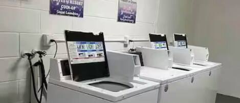 Een hotelwasserij met meerdere wasmachines en drogers, een waterfontein en informatieposters aan de muur.