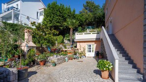 Un patio con suelo de piedra, plantas en macetas, una escalera y un edificio con balcones.