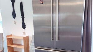 Uma geladeira de aço inoxidável com duas portas e uma gaveta de freezer, uma cadeira de madeira e um banquinho de metal.