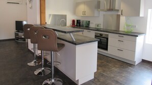 Uma cozinha moderna com uma ilha central, banquetas, eletrodomésticos de aço inoxidável e iluminação pendente.