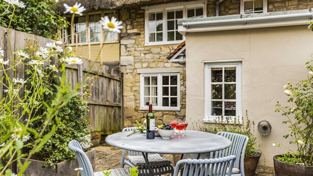 A round table with chairs in a garden area, a bottle, and glasses of red drink. - Willow Cottage, Chilmark, Wiltshire (Chilmark)