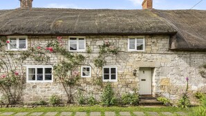 A stone house with a thatched roof, three windows, and a door. - Willow Cottage, Chilmark, Wiltshire (Chilmark)