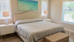 A bedroom with a bed, two nightstands, a bench, and a large painting of a beach scene. - Bradenton Gem - Beaches, Downtown, IMG Academy, New Pool! (Bradenton)