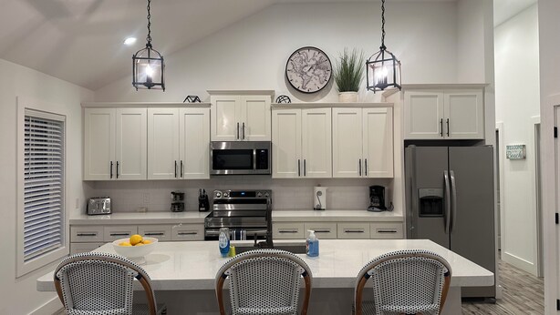 A modern kitchen with white cabinets, a central island with bar stools, a microwave, oven, and refrigerator. - Bradenton Gem - Beaches, Downtown, IMG Academy, New Pool! (Bradenton)