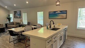A modern kitchen with a central island, white cabinetry, and a dining area with a round table and chairs. - Bradenton Gem - Beaches, Downtown, IMG Academy, New Pool! (Bradenton)