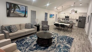 A spacious living room with a large coffee table, a sofa, and a dining area with a kitchen in the background. - Bradenton Gem - Beaches, Downtown, IMG Academy, New Pool! (Bradenton)