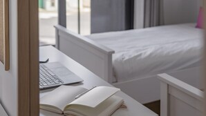 A bedroom with a white bed, a desk with a laptop and an open book, and a window with a view of the outside. - In the Funchal Centre, with outdoor area - Pena II (Funchal)