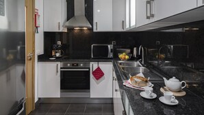 A modern kitchen with white cabinets, a stainless steel range hood, a microwave, and a sink with a stainless steel faucet. - In the Funchal Centre, with outdoor area - Pena II (Funchal)