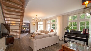 A spacious living room with a sofa, a piano, a TV, and a staircase. - house 200 m2 4 bedrooms 4 bathrooms for 10 people in the valley of the kings (Azay-sur-Cher)