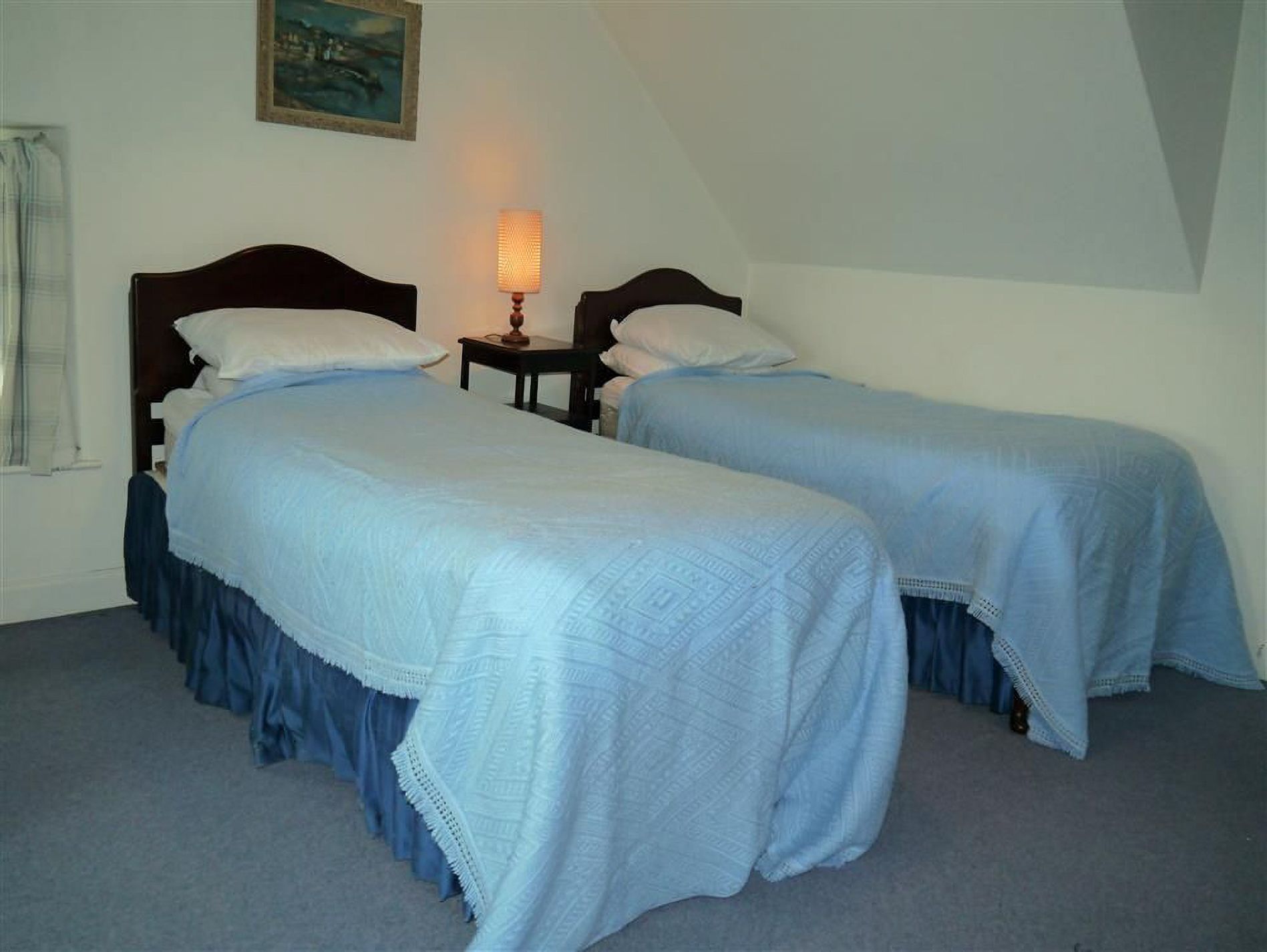 A room with two beds, a nightstand, a lamp, and a painting on the wall.