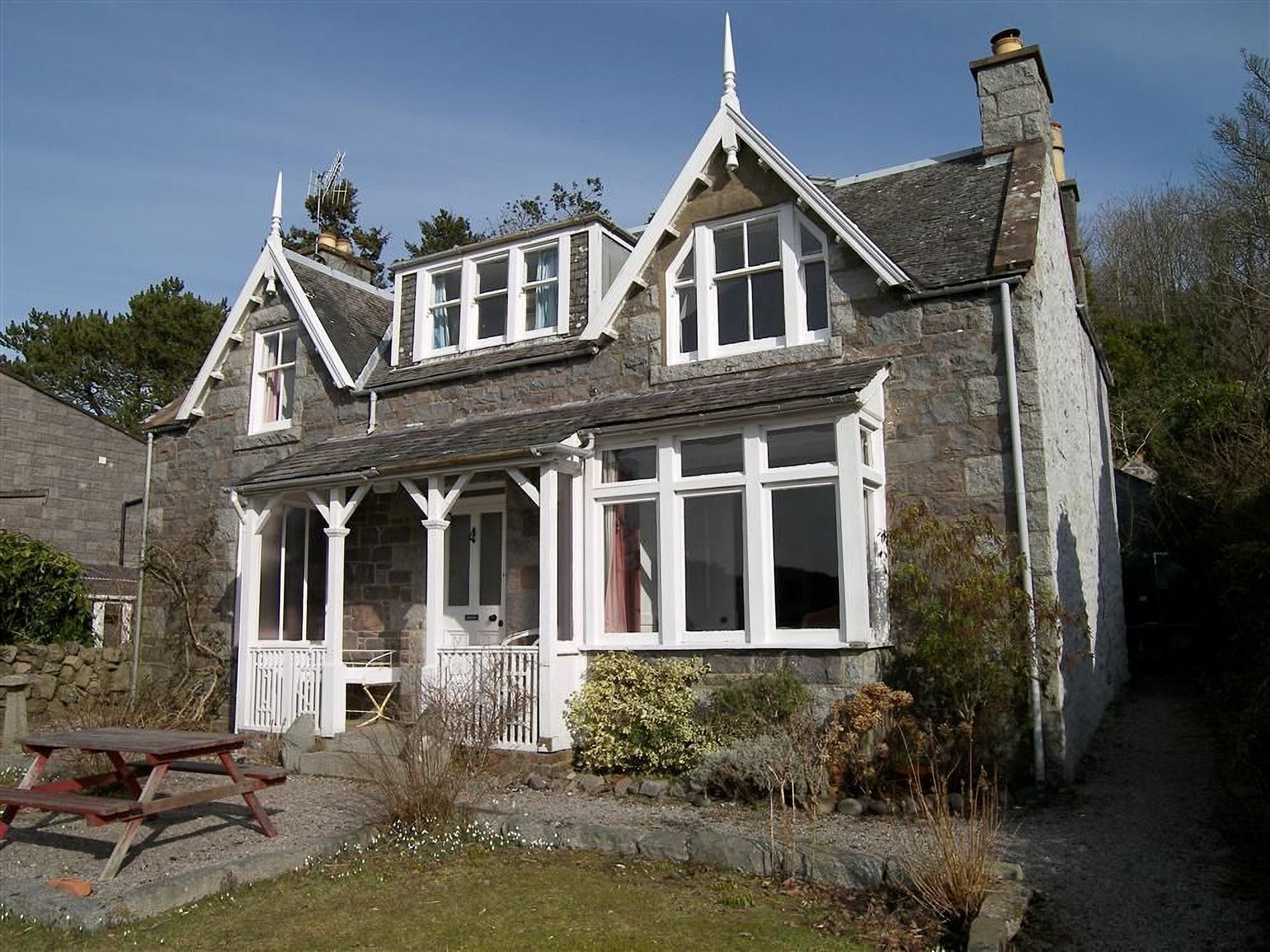 A stone house with a gabled roof, a porch with a bench, and a stone wall.