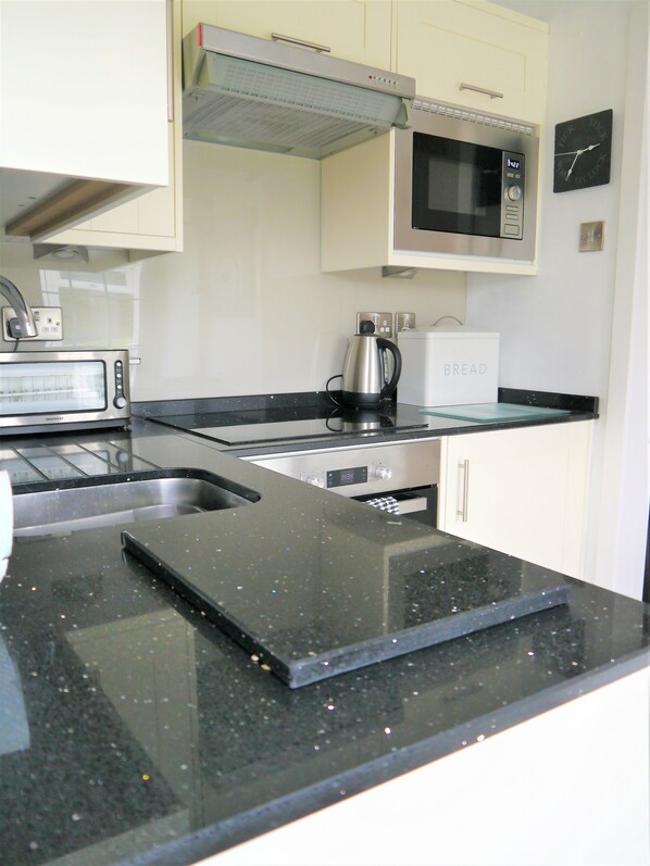 A modern kitchen with a stainless steel toaster, a kettle, a microwave, and a bread box. - St Marys Cottage - a cottage that sleeps 4 guests in 2 bedrooms (Rockcliffe, Dalbeattie)