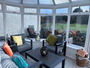 Une véranda dotée d’un espace salon avec des canapés et une table, un panier en osier, et donnant sur un jardin.