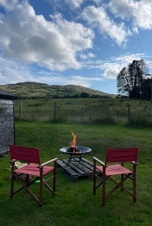 A grassy outdoor area with a fire pit and two chairs.