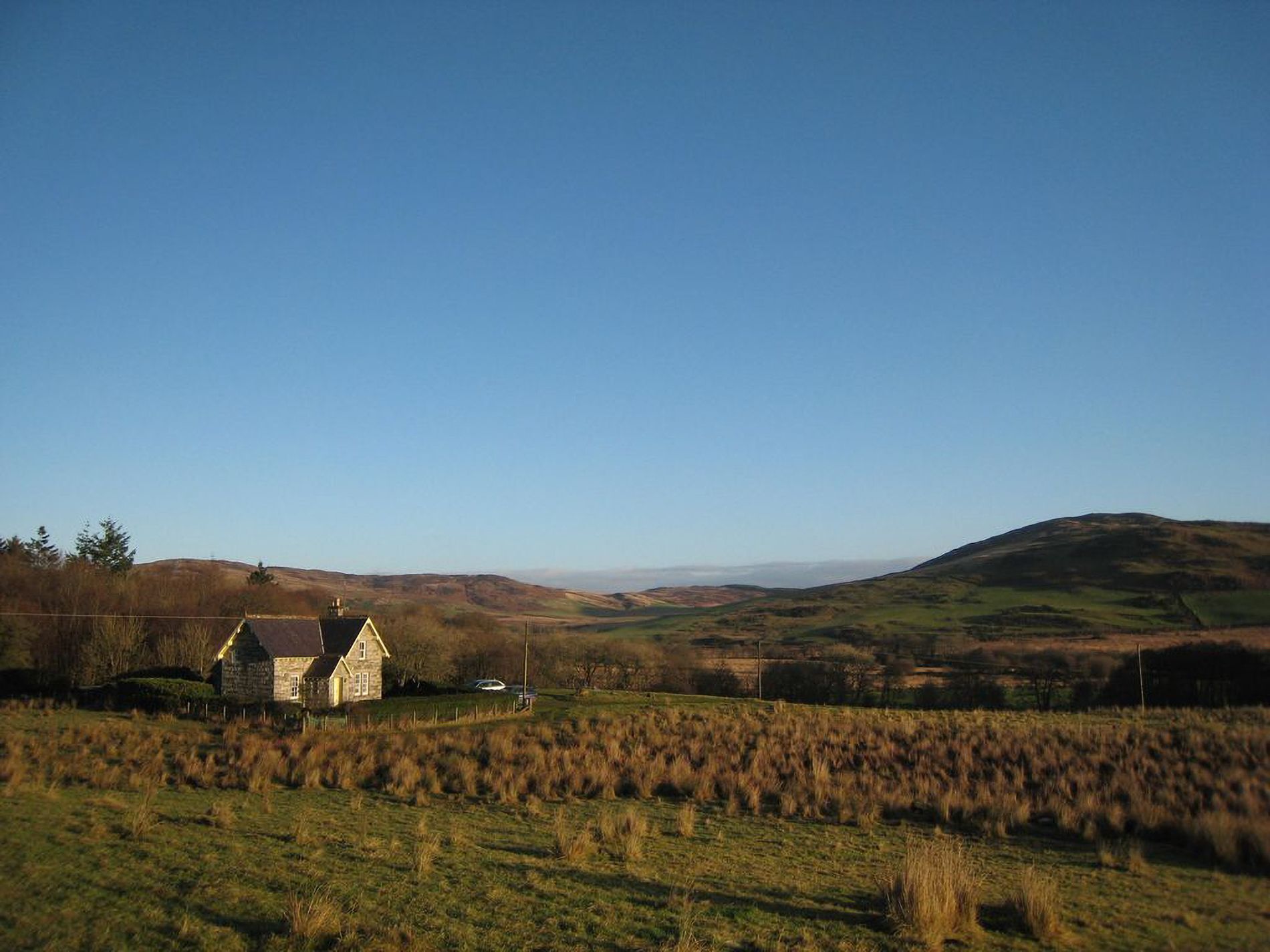 A rural landscape with a stone house, rolling hills, and a clear sky.