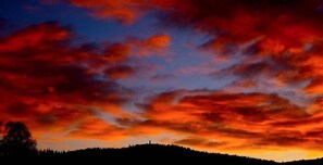 A sunset over a hilly landscape with a silhouette of a hill and a small structure.