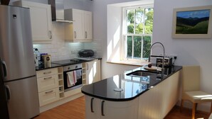 A modern kitchen with white cabinetry, a black countertop, and a window providing natural light. - Rusko Stables -  an apartment that sleeps 6 guests  in 3 bedrooms (Gatehouse Of Fleet)