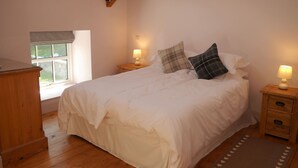 A bedroom with a large bed, wooden headboard, two bedside tables with lamps, a window with blinds, and a wooden dresser. - Rusko Stables -  an apartment that sleeps 6 guests  in 3 bedrooms (Gatehouse Of Fleet)
