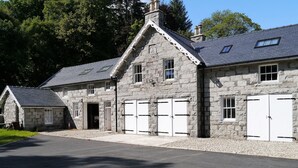 A stone building with a gabled roof, multiple garage doors, and a paved driveway. - Rusko Stables -  an apartment that sleeps 6 guests  in 3 bedrooms (Gatehouse Of Fleet)