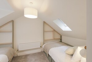 A bedroom with two beds, a skylight, a radiator, and a ceiling light fixture.