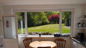 A kitchen with a dining table and chairs, a window with a view of a garden, and a white refrigerator.
