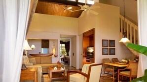 A spacious living area with a high ceiling, wooden beams, a large sofa, a dining table with chairs, and a view of the outdoors. - Stunning 1BR Condo with Garden View (Princeville)