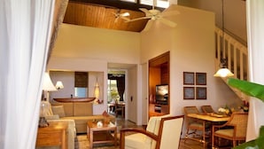 A spacious living area with a high ceiling, wooden beams, a large sofa, a dining table with chairs, and a view of the outdoors. - Stunning 1BR Condo at Pismo Beach (Princeville)